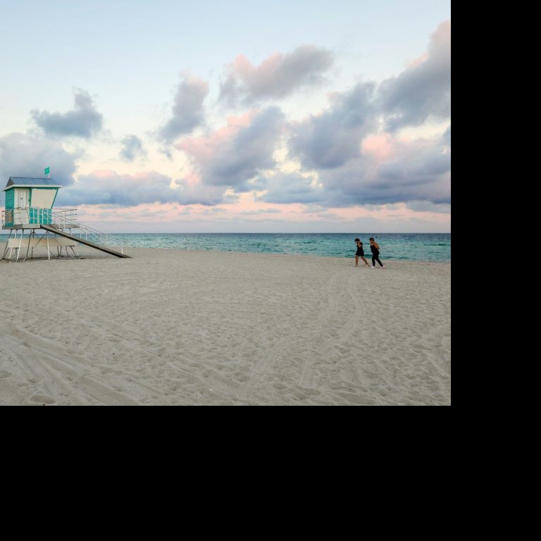 Beach Lifeguard tower on a beach with people walking along the shoreline under cloudy skies.