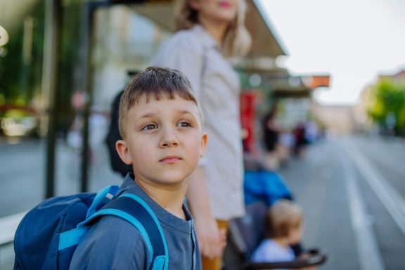 Young boy with backpack gazes thoughtfully while waiting at a bus stop.